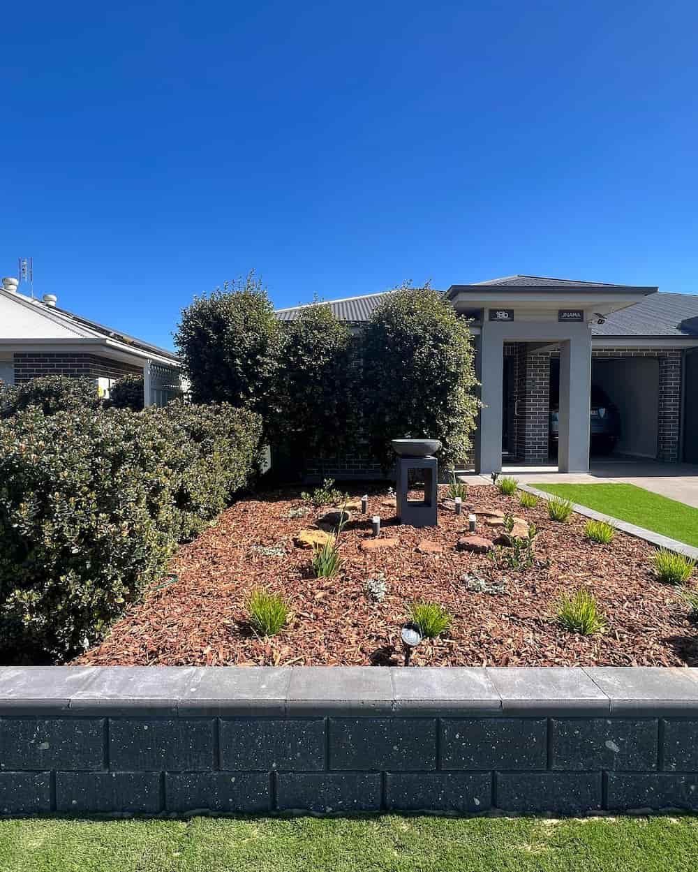 A Brick Wall Surrounds a Garden in Front of A House — Creative Spaces Landscaping in Dubbo, NSW