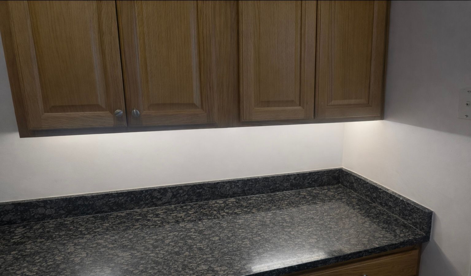 Kitchen corner with wooden cabinets, gray countertop, and under-cabinet lighting.
