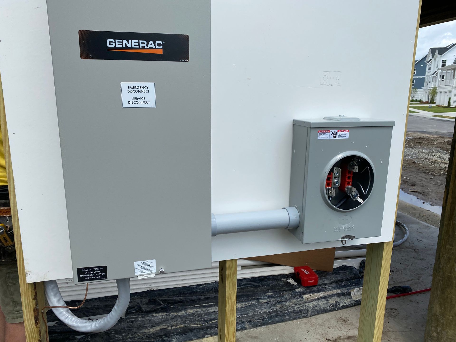 Generac generator and meter box mounted on a wooden frame, outdoors. Conduit connects the two.
