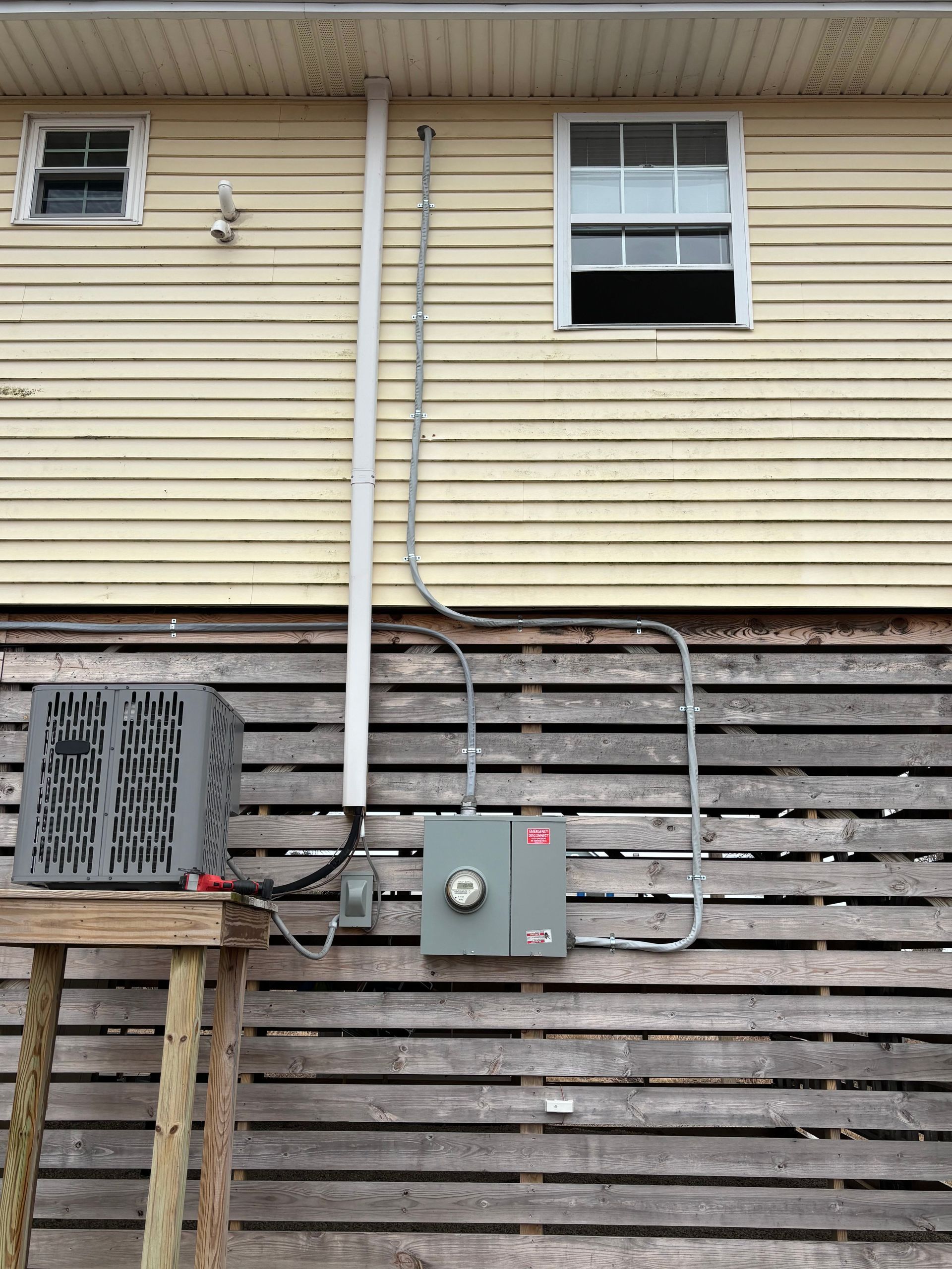 Exterior house wall with electrical meter, gray service panel, and conduit.