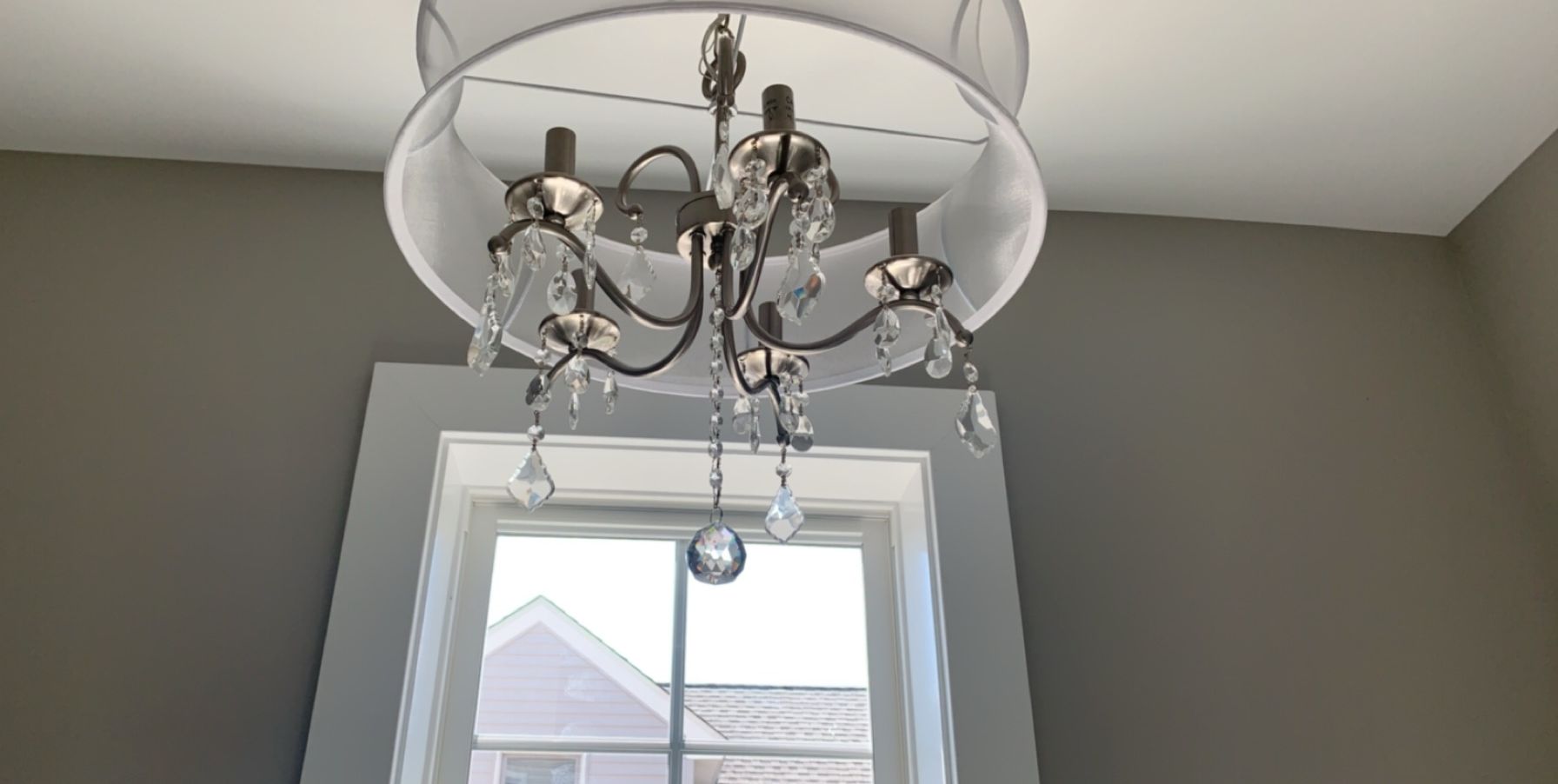 Chandelier hanging near a window, grey walls, white trim and ceiling.