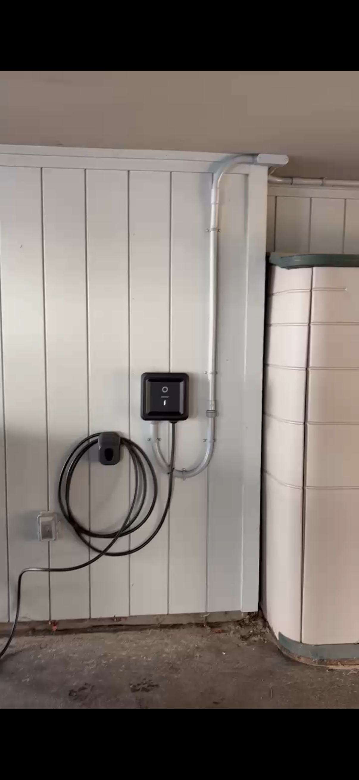 Electric vehicle charger mounted on a white wall with a coiled charging cable.