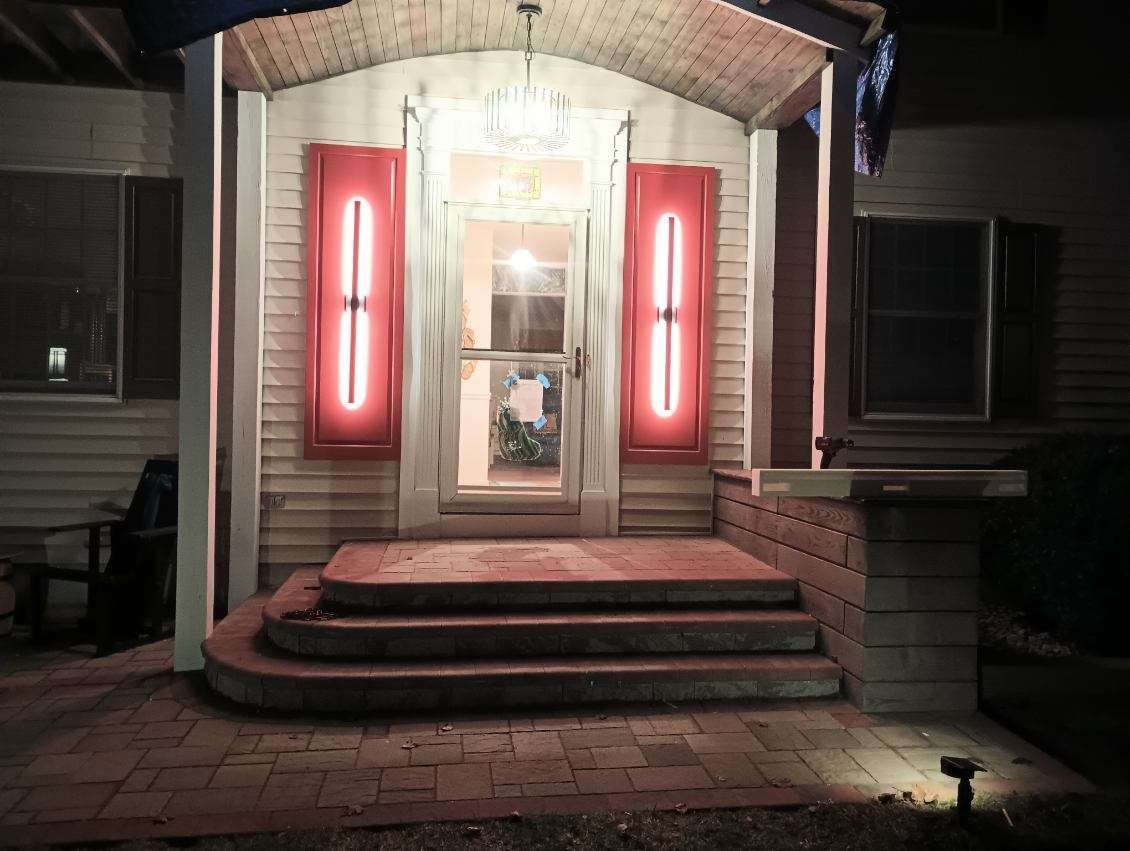 Lit entryway of a house at night, featuring a glass door, red accents, and brick steps.