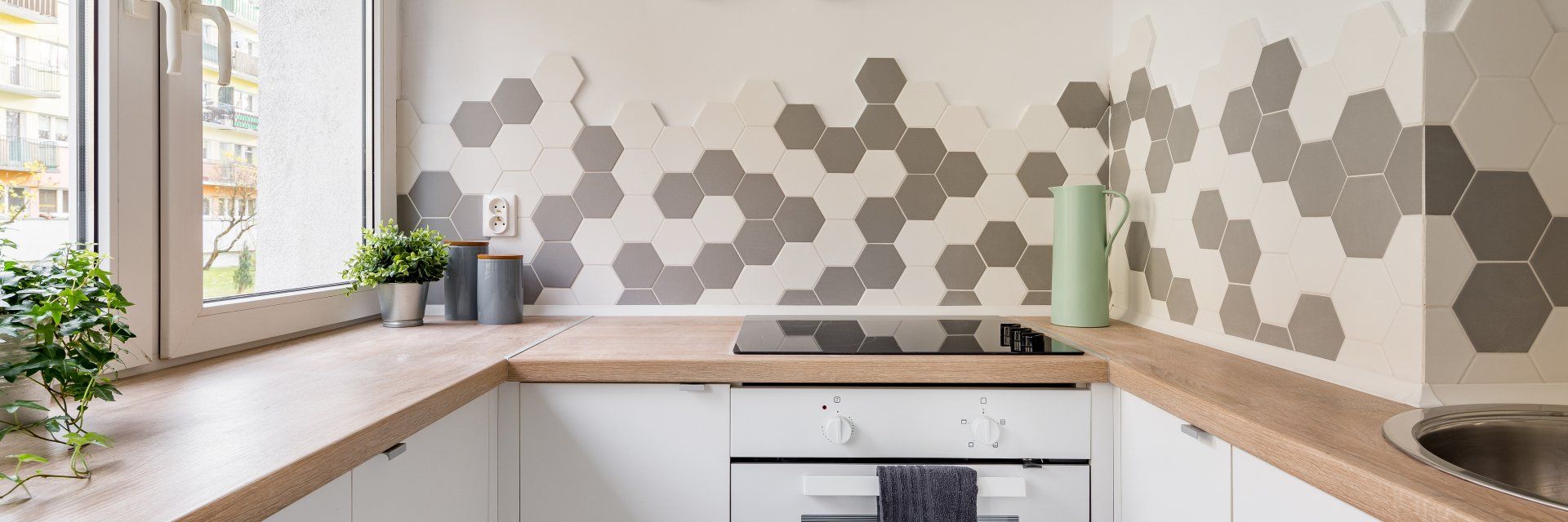 Panorama of kitchen in scandinavian style with white cabinets, wooden countertop and hexagonal wall tiles