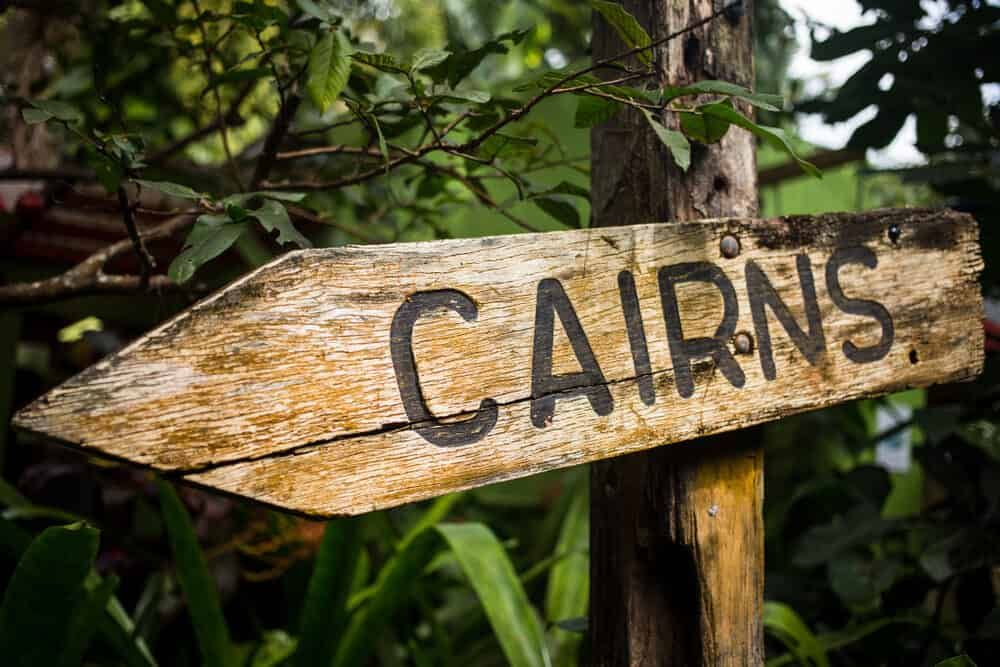 A Wooden Sign Pointing To Cairns Is Surrounded By Trees — FNQ Professional Cleaning Services In Cairns, QLD