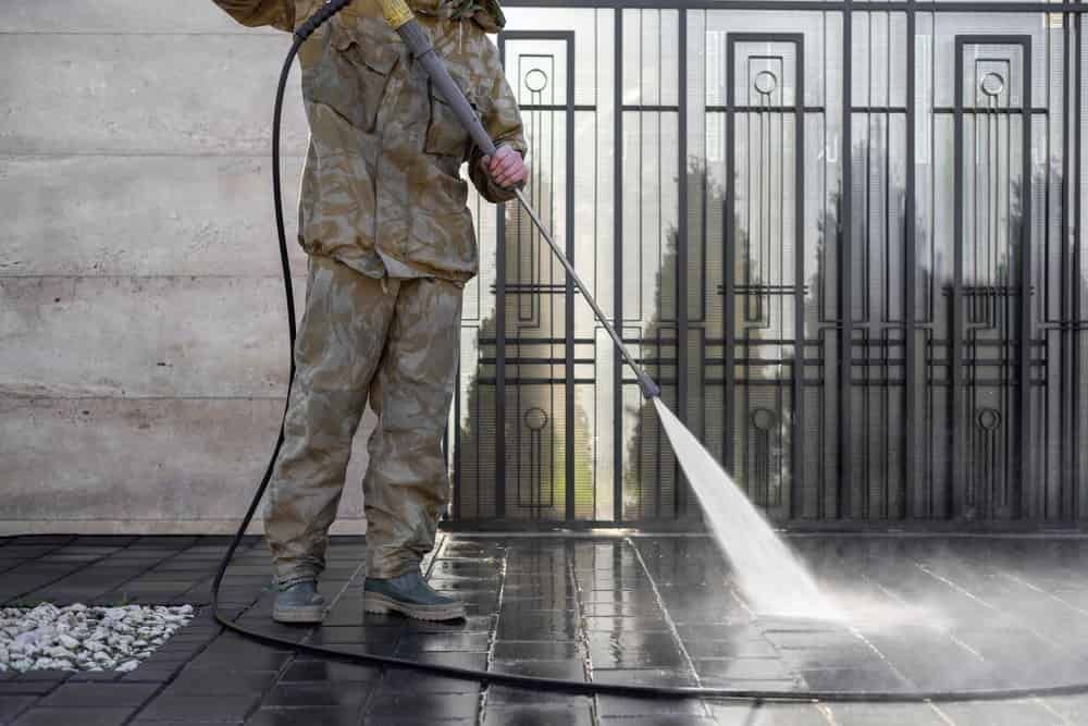 A Man Is Using A High Pressure Washer To Clean A Fence — FNQ Professional Cleaning Services In Mooroobool, QLD