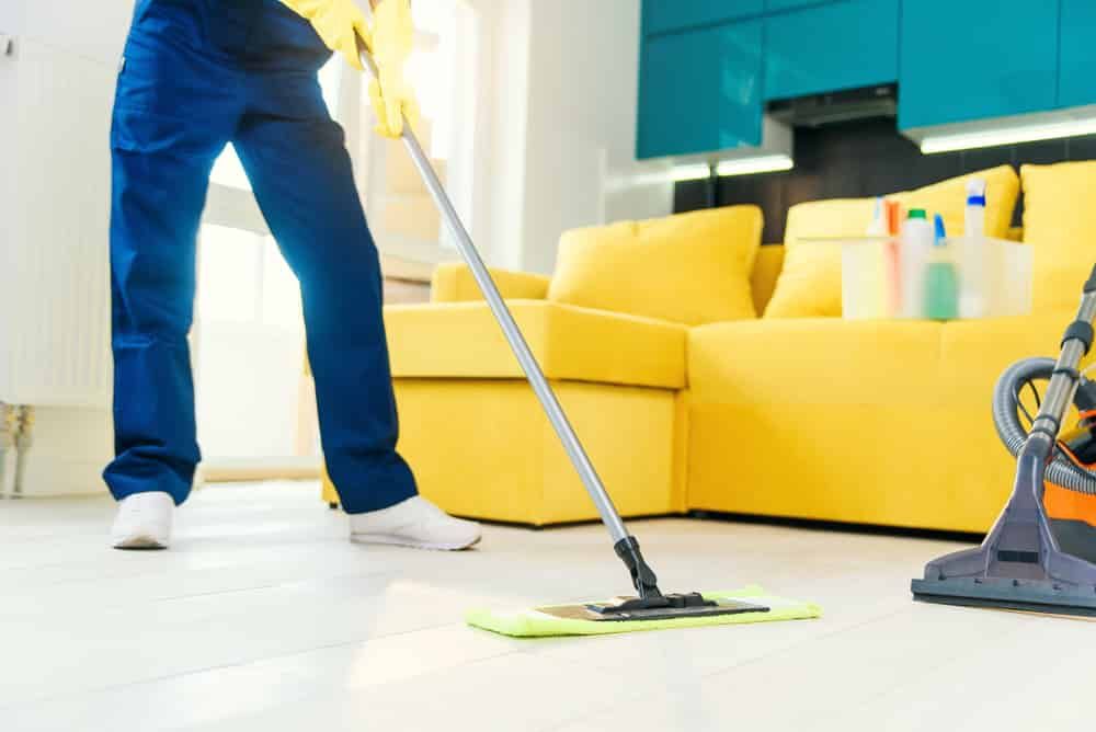 A Person Is Mopping The Floor In A Living Room — FNQ Professional Cleaning Services In Mooroobool, QLD