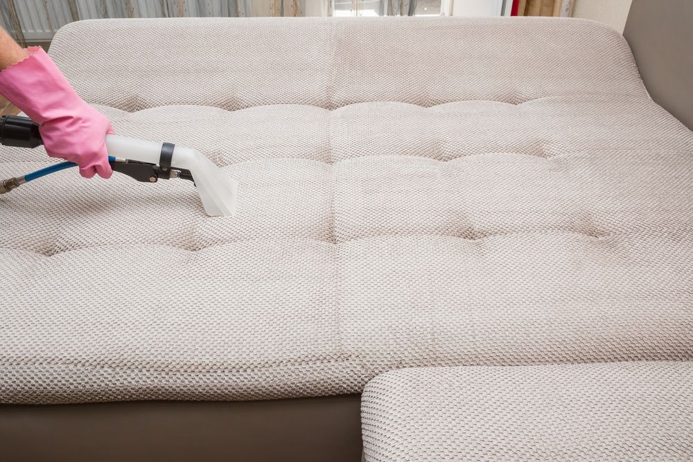 Person in Pink Gloves Vacuuming a Light-colored, Tufted Couch — FNQ Cleaning Services in Kanimbla, QLD