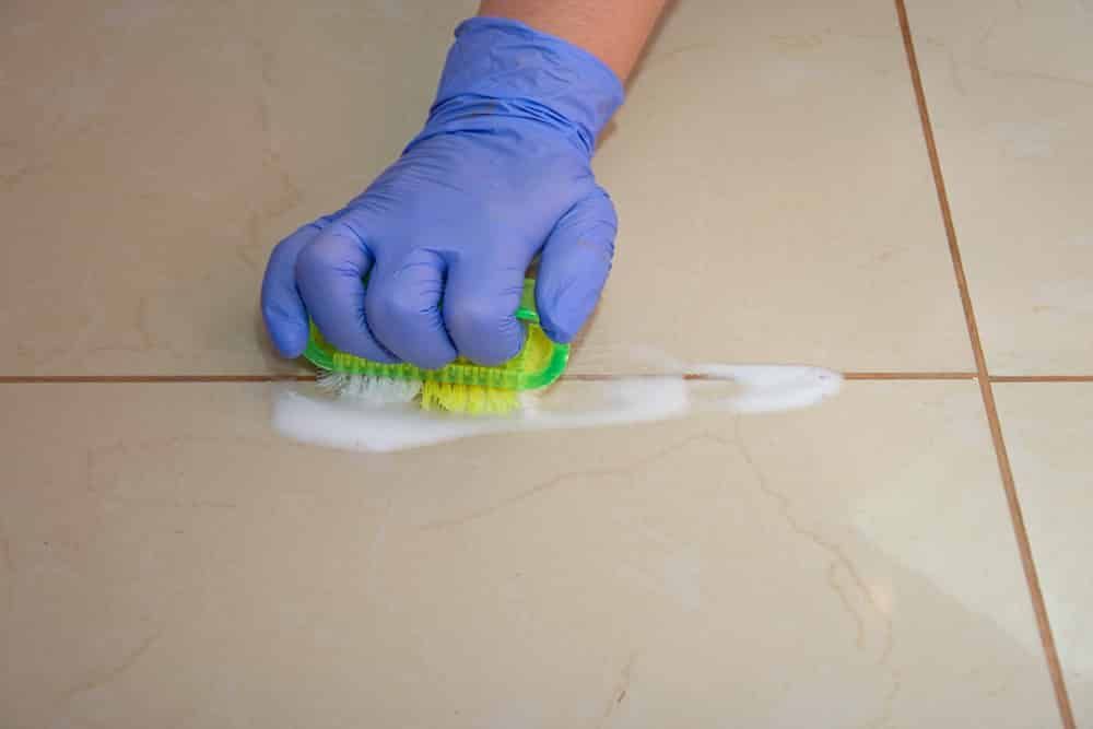 A Person Wearing Gloves Is Cleaning A Tile Floor With A Sponge — FNQ Professional Cleaning Services In Mooroobool, QLD