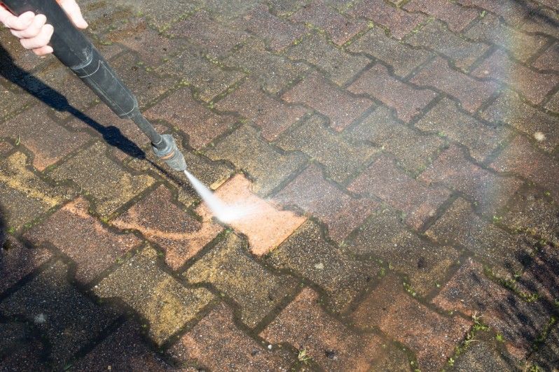 A Person is Using a High Pressure Washer to Clean a Brick Sidewalk — FNQ Professional Cleaning Services In Mooroobool, QLD