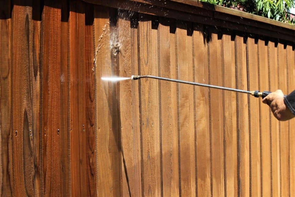 A Person is Cleaning a Wooden Fence With a High Pressure Washer — FNQ Professional Cleaning Services In Mooroobool, QLD