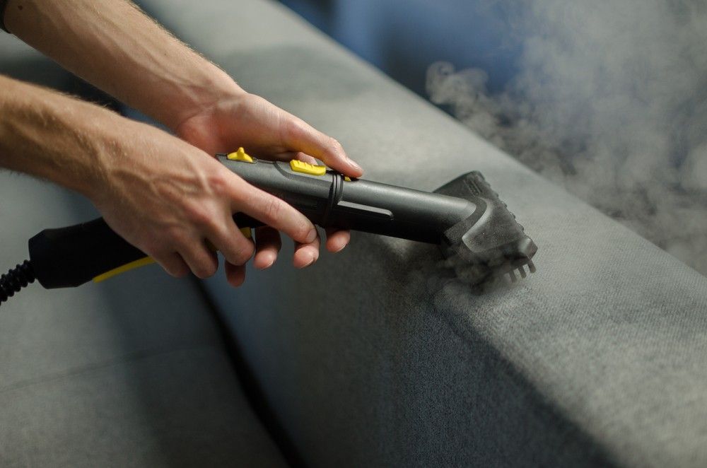 A Person is Cleaning a Couch With a Steam Cleaner — FNQ Professional Cleaning Services In Mooroobool, QLD