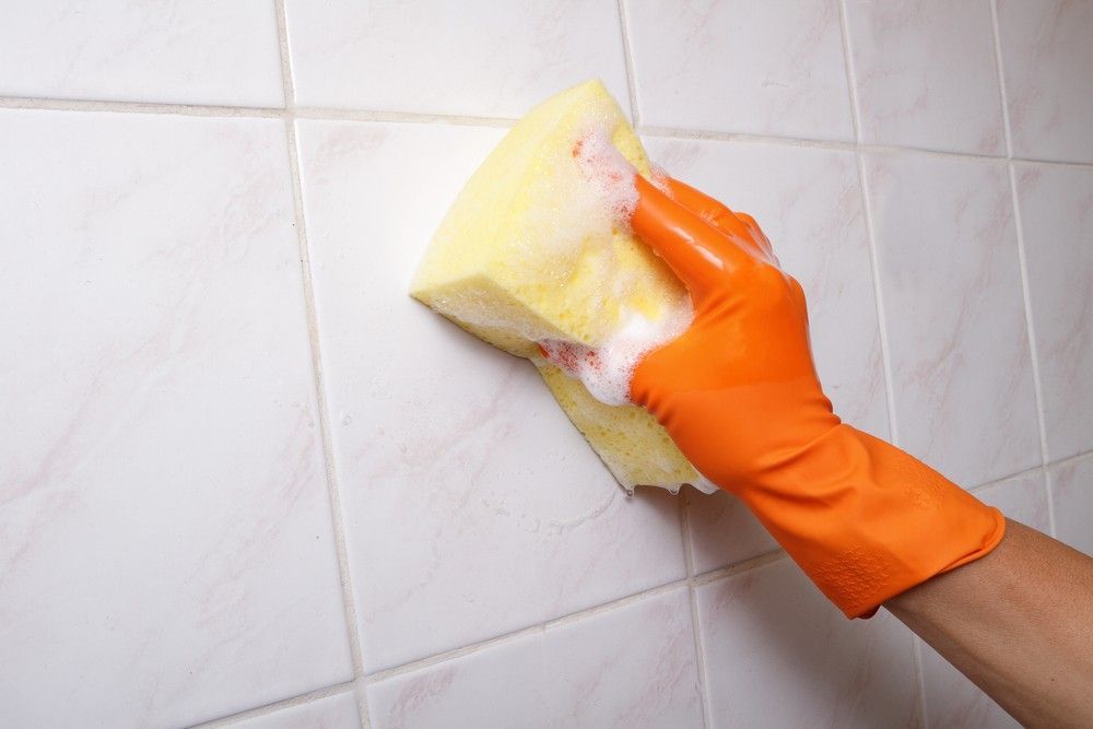 A Person Wearing Orange Gloves is Cleaning a Tile Wall With a Sponge — FNQ Professional Cleaning Services In Mooroobool, QLD