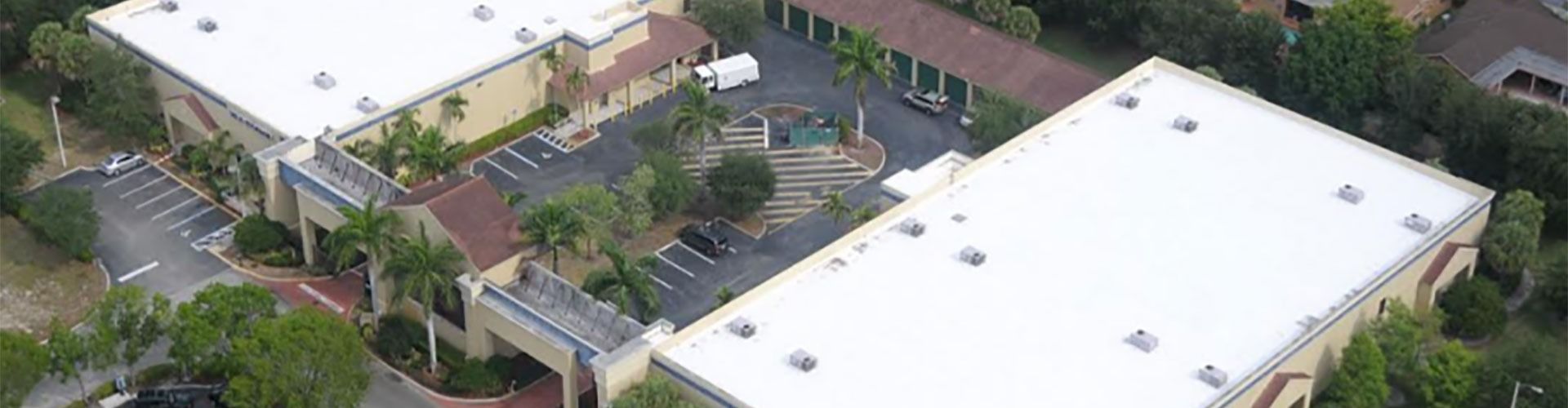 An aerial view of a group of buildings with white roofs surrounded by trees.