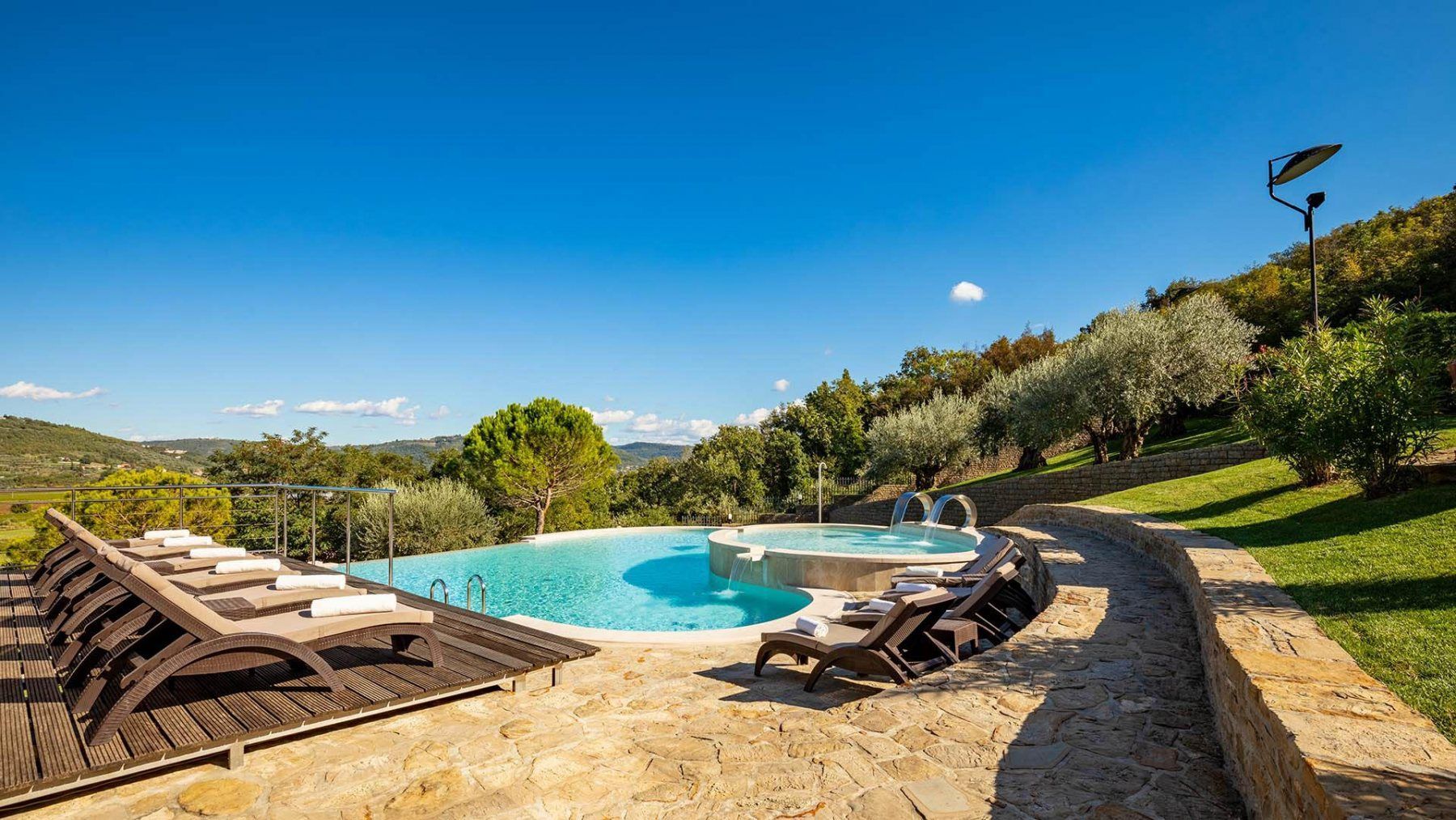 Vista a bordo piscina con sedie a sdraio, alberi e cielo azzurro.