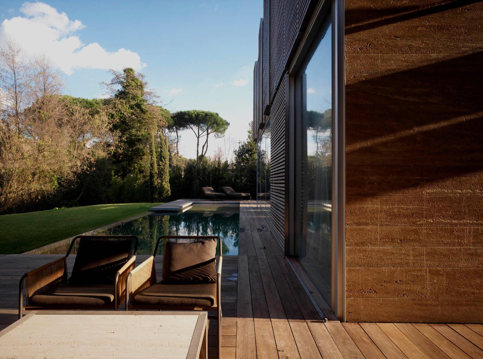Casa moderna con terrazza in legno, piscina e area salotto all'aperto nelle giornate di sole.