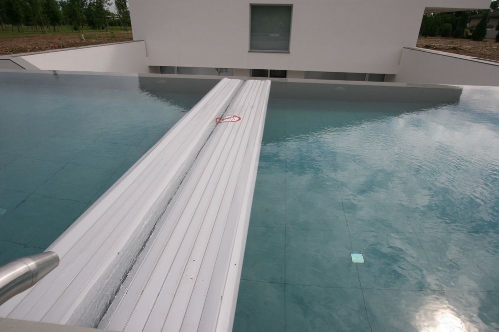 Piscina con copertura retrattile. Edificio bianco sullo sfondo.