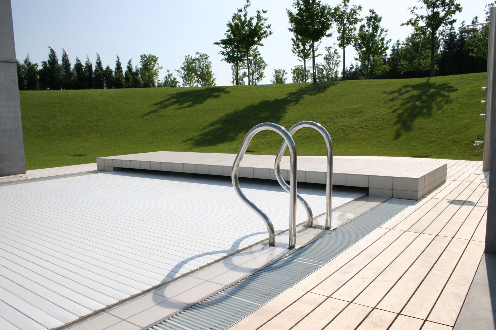 Piscina con copertura bianca chiusa, scaletta metallica, prato verde sullo sfondo.