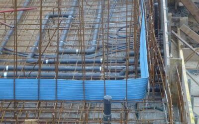 Griglia di barre d'armatura con tubi neri e bordi blu in casseforme di cemento, probabilmente un cantiere edile.