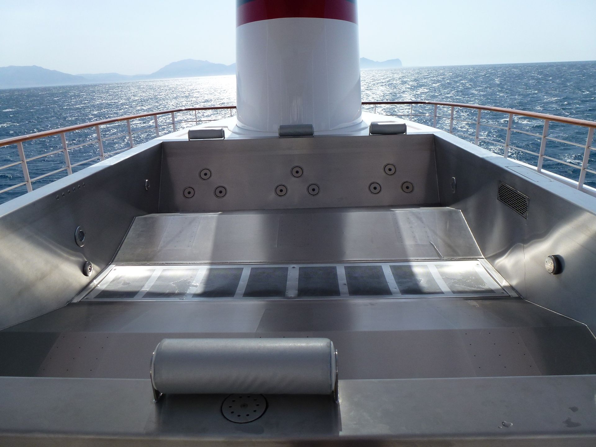 A bordo di una nave, una jacuzzi in acciaio inossidabile con un camino sullo sfondo, di fronte al mare.