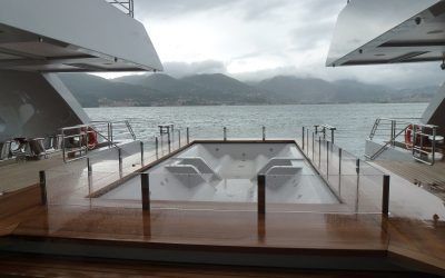 Ponte di yacht di lusso con vasca idromassaggio e vista panoramica sull'acqua e sulle montagne.