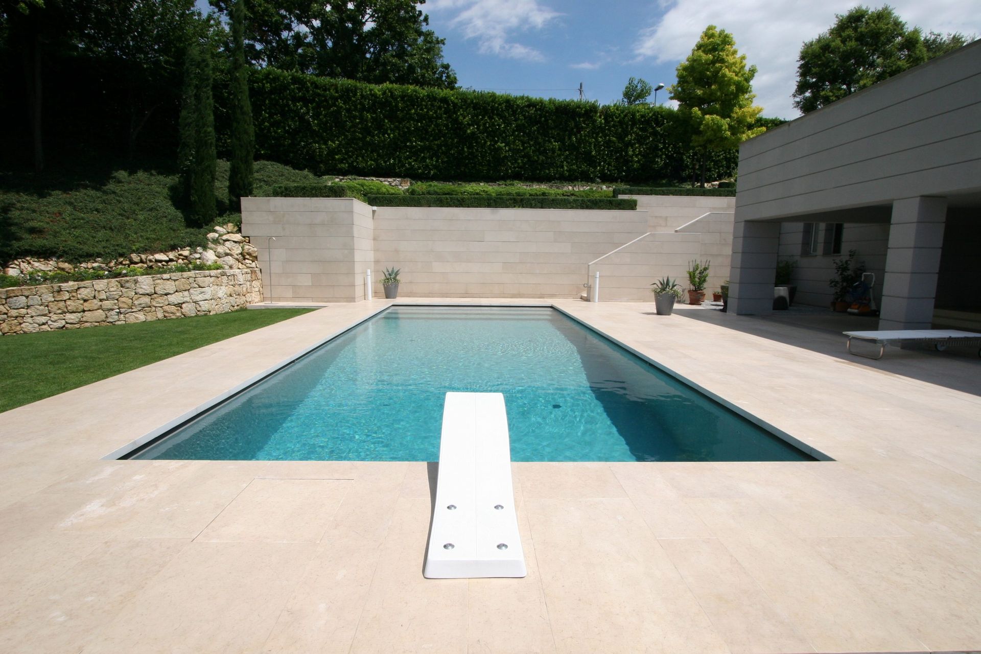 Piscina con trampolino, circondata da patio in pietra, prato e giardino.