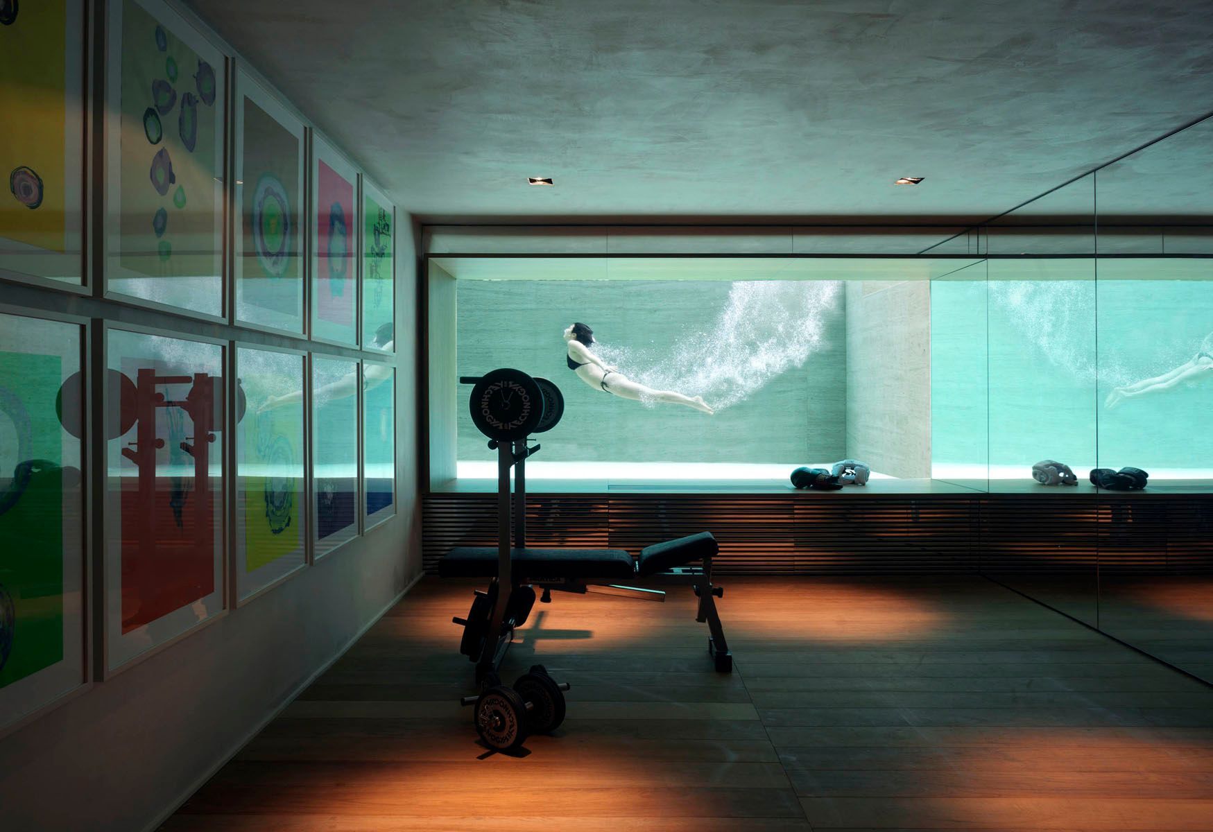 Palestra con panca pesi e piscina adiacente con nuotatore. Opera d'arte alla parete.