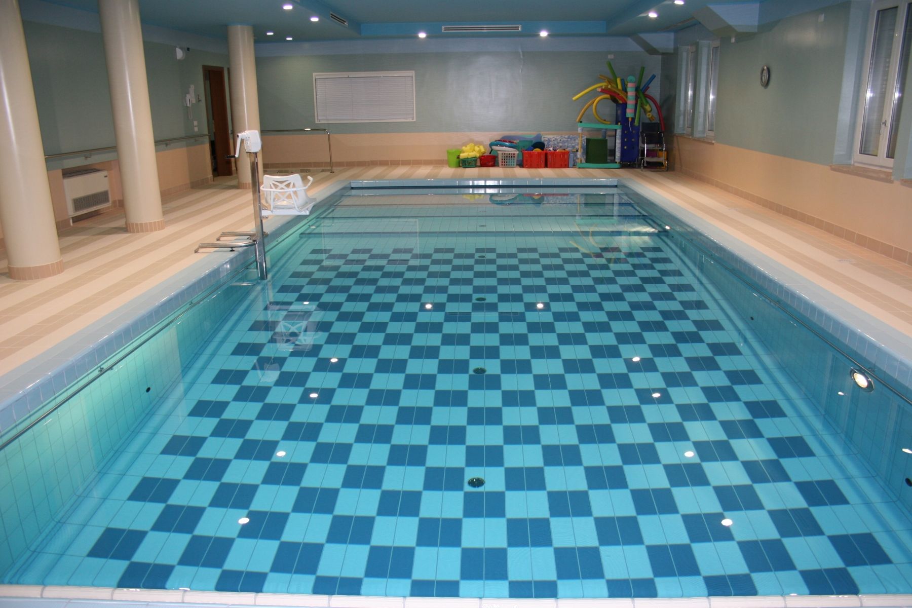 Piscina coperta con piastrelle a scacchi blu e bianche, pareti beige.