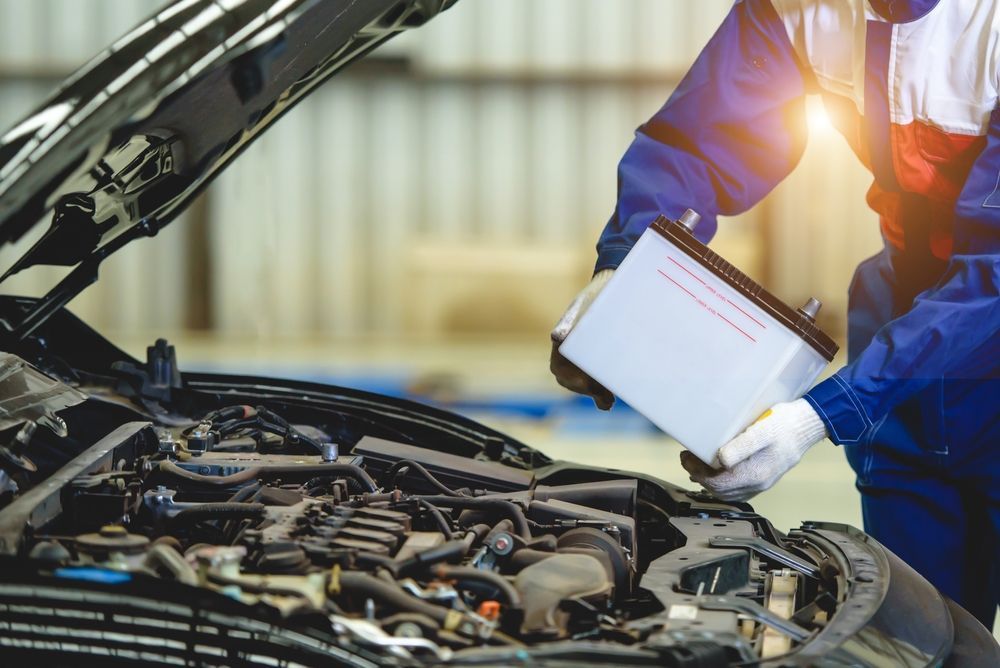 A mechanic is changing a car battery in a garage.