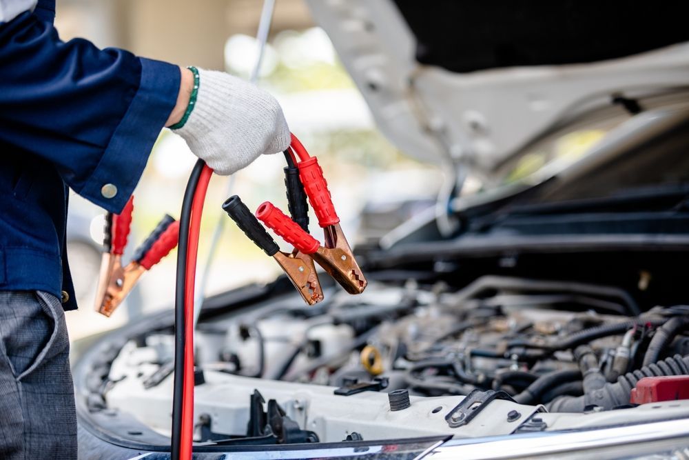 A man is holding a pair of jumper cables in front of a car.