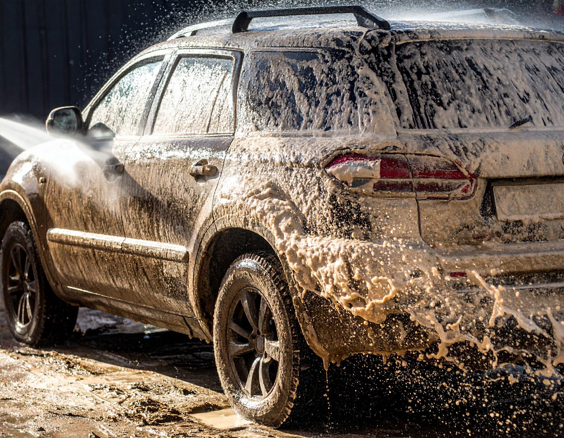Mud-splattered SUV being sprayed with water at a car wash