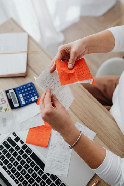 Person examining receipts and small red cards on a desk with a calculator and laptop.