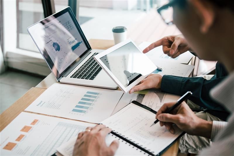 People reviewing financial data on a laptop, tablet, and paper documents.