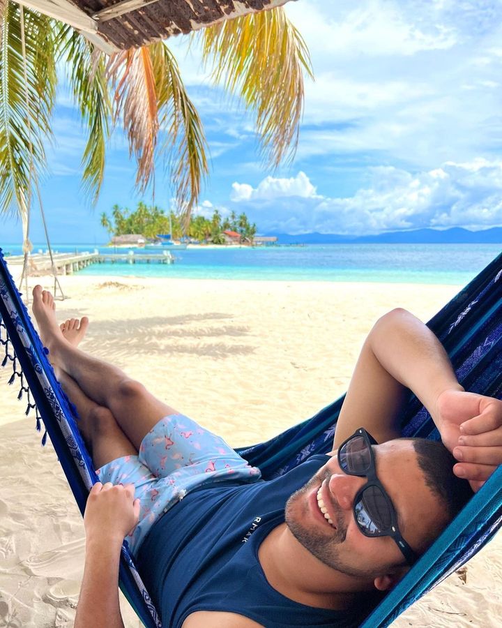 A man wearing sunglasses is laying in a hammock on the beach.