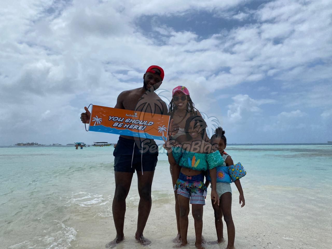 A family is standing on a beach holding a sign.