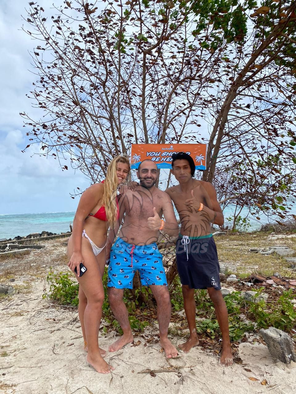 A man and two women are posing for a picture on a beach.