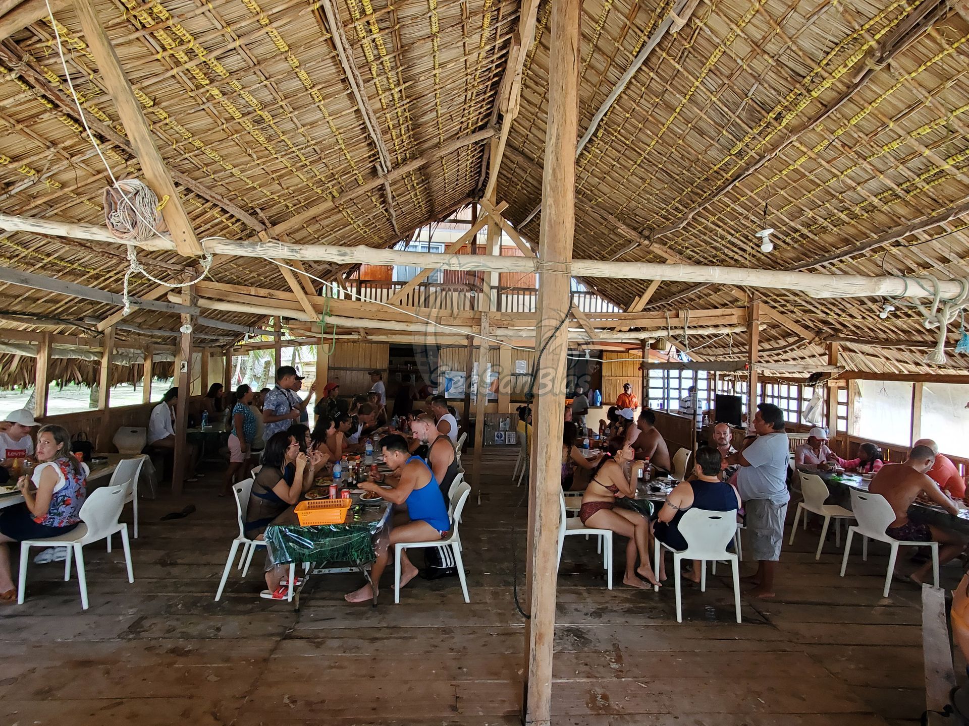 a group of people are sitting at tables under a thatched roof