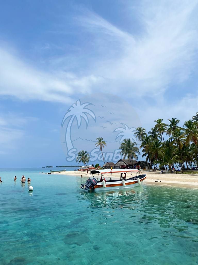 A boat is floating on the water near a beach with palm trees. San Blas Islands Guna Yala San Blas Tours