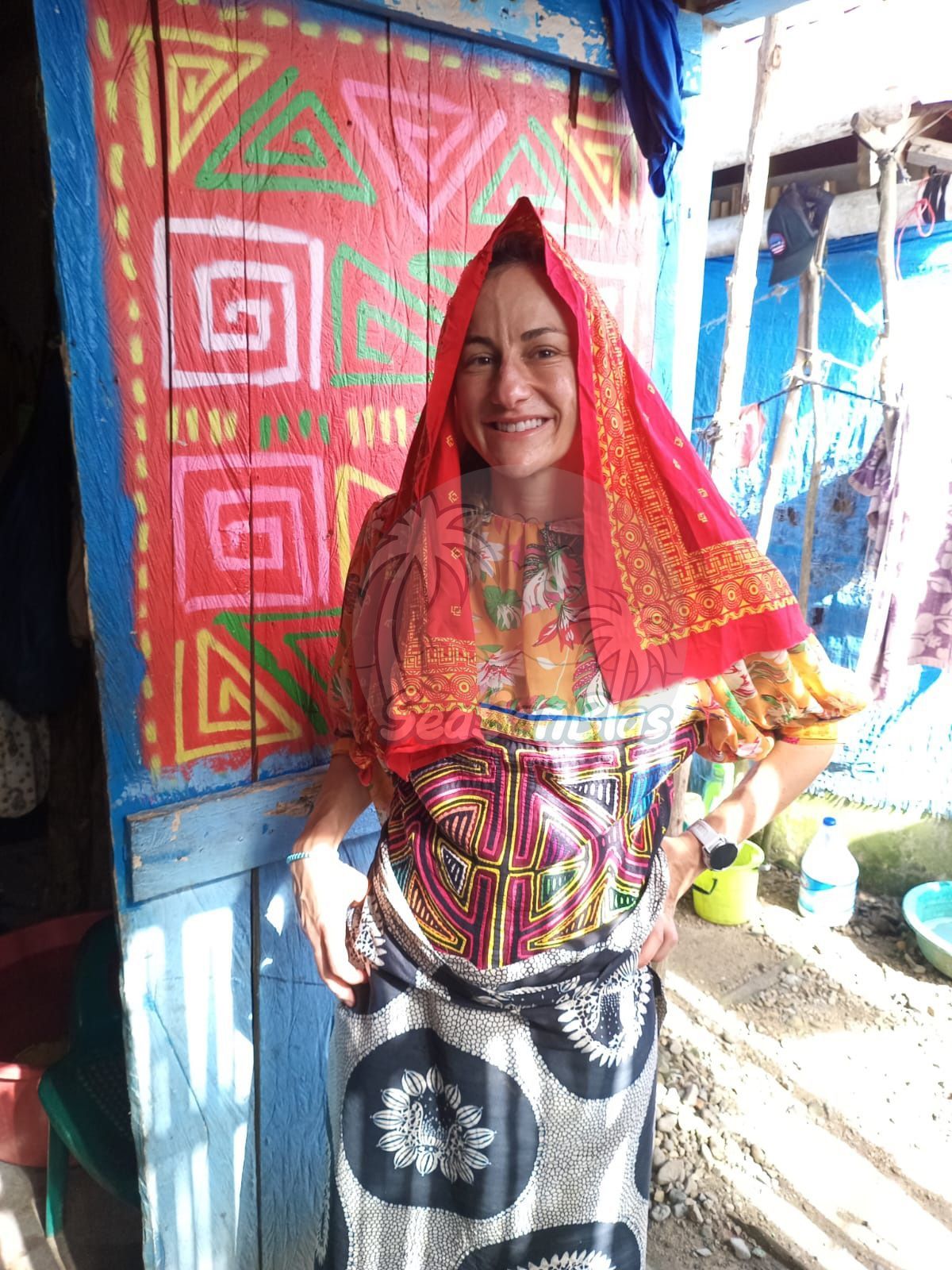 A woman in a colorful dress is standing in front of a colorful wall.