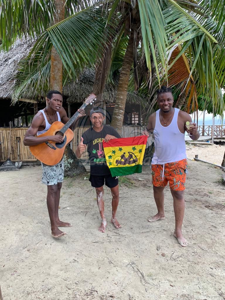 Three men are standing on a beach holding a flag and a guitar. San Blas Islands Guna Yala San Blas Tours