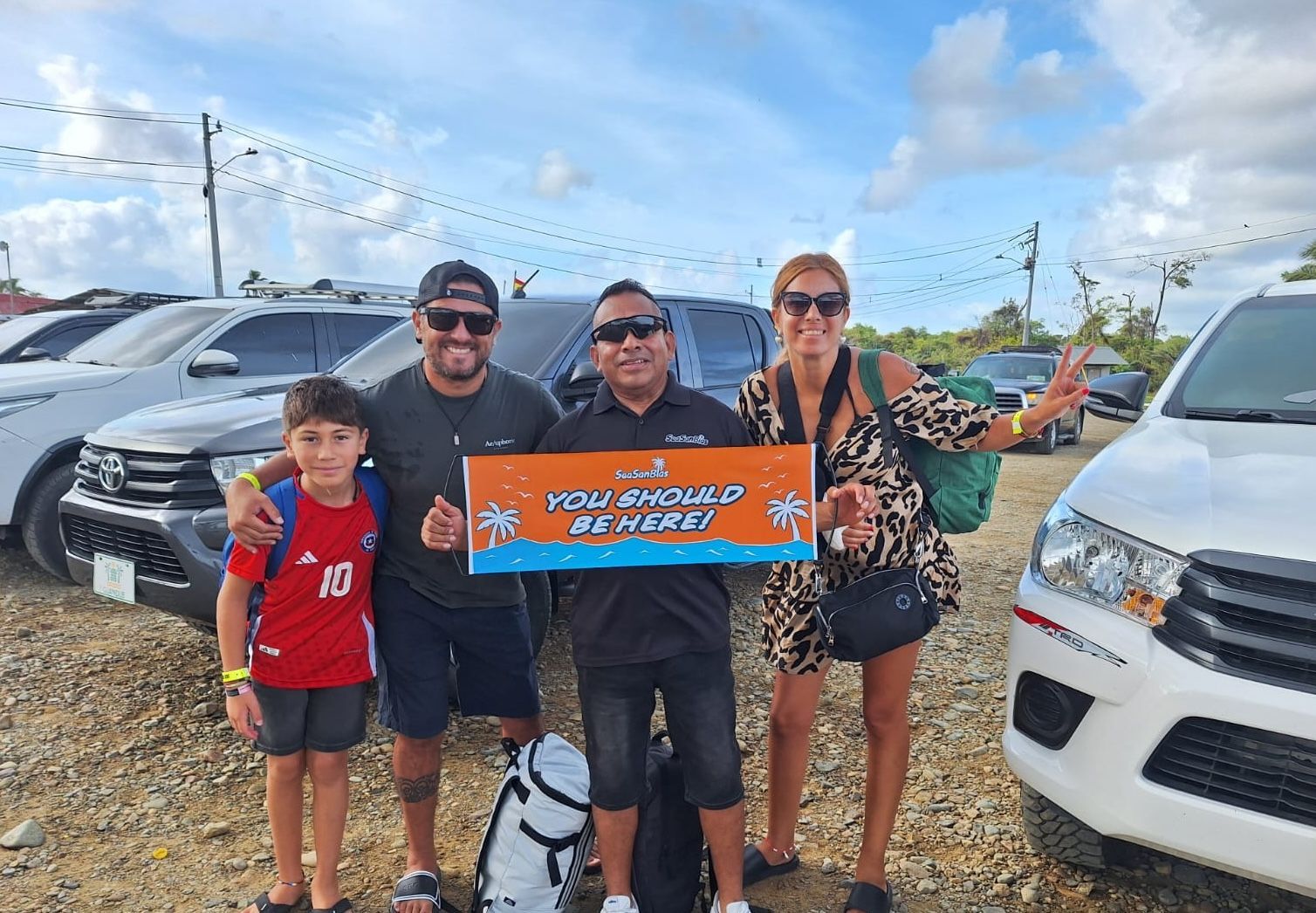Happy customers smiling on the beach holding up banner that says Sea San Blas