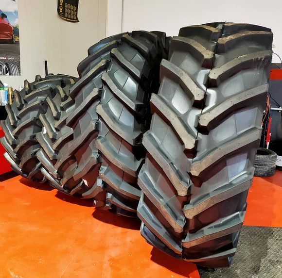 Fila di grandi pneumatici neri da trattore su un pavimento arancione all'interno di un negozio.