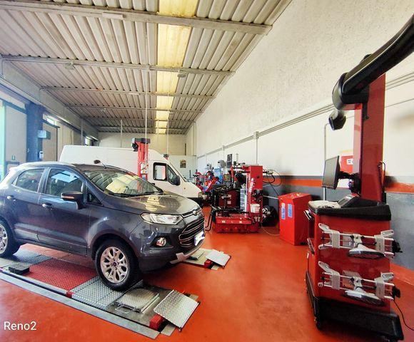 Auto su un ponte sollevatore all'interno di un garage. Attrezzatura per l'allineamento, furgone bianco sullo sfondo.