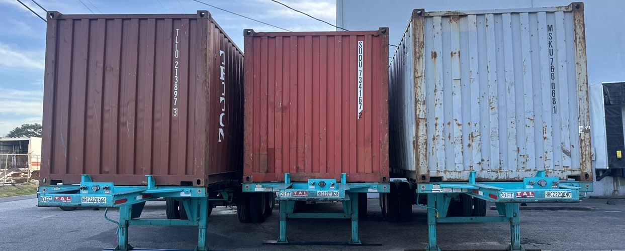 Three shipping containers on teal-colored chassis in an outdoor setting.