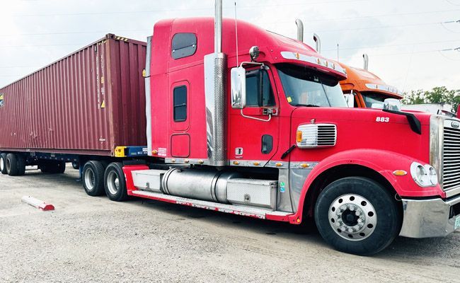 Red semi-truck with cargo container parked on gravel.
