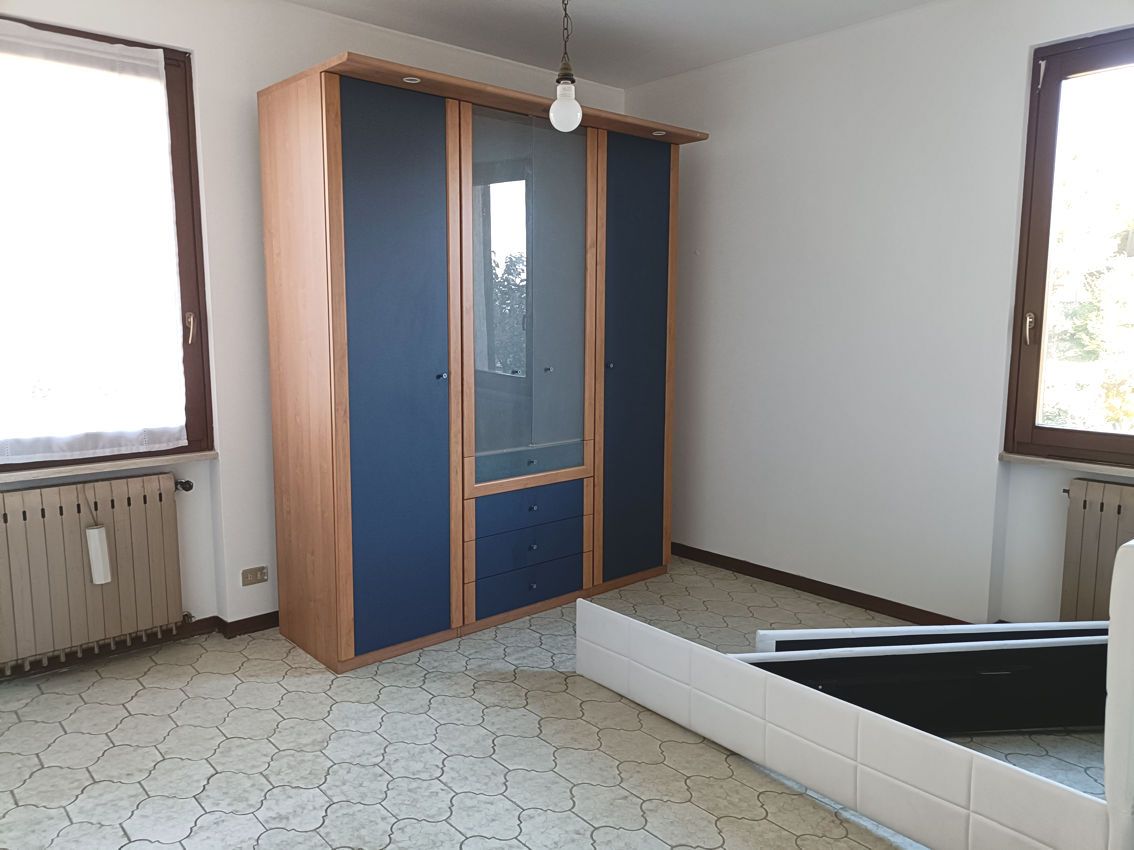 Una stanza vuota con un armadio blu e due finestre.