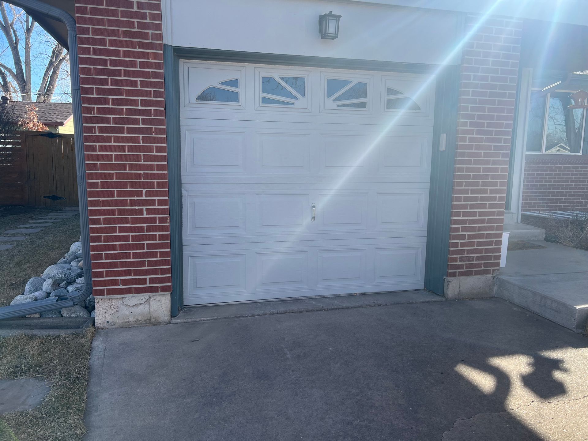 White garage door on a brick building with a concrete driveway. Bright sunlight.