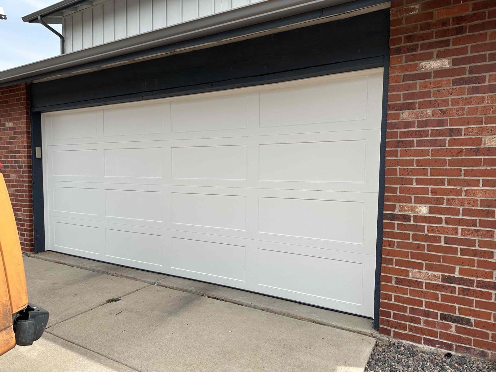 A white garage door is sitting in front of a brick building.