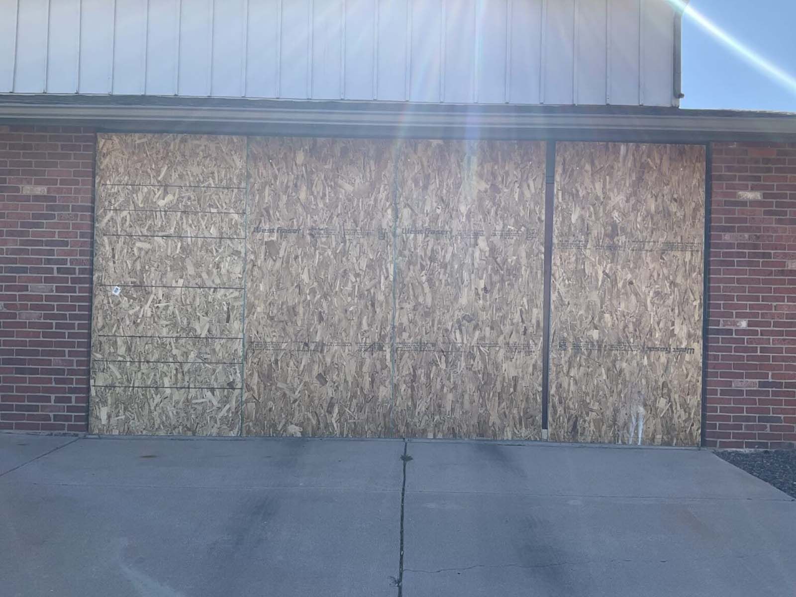 A brick building with plywood covering the windows and a concrete sidewalk.