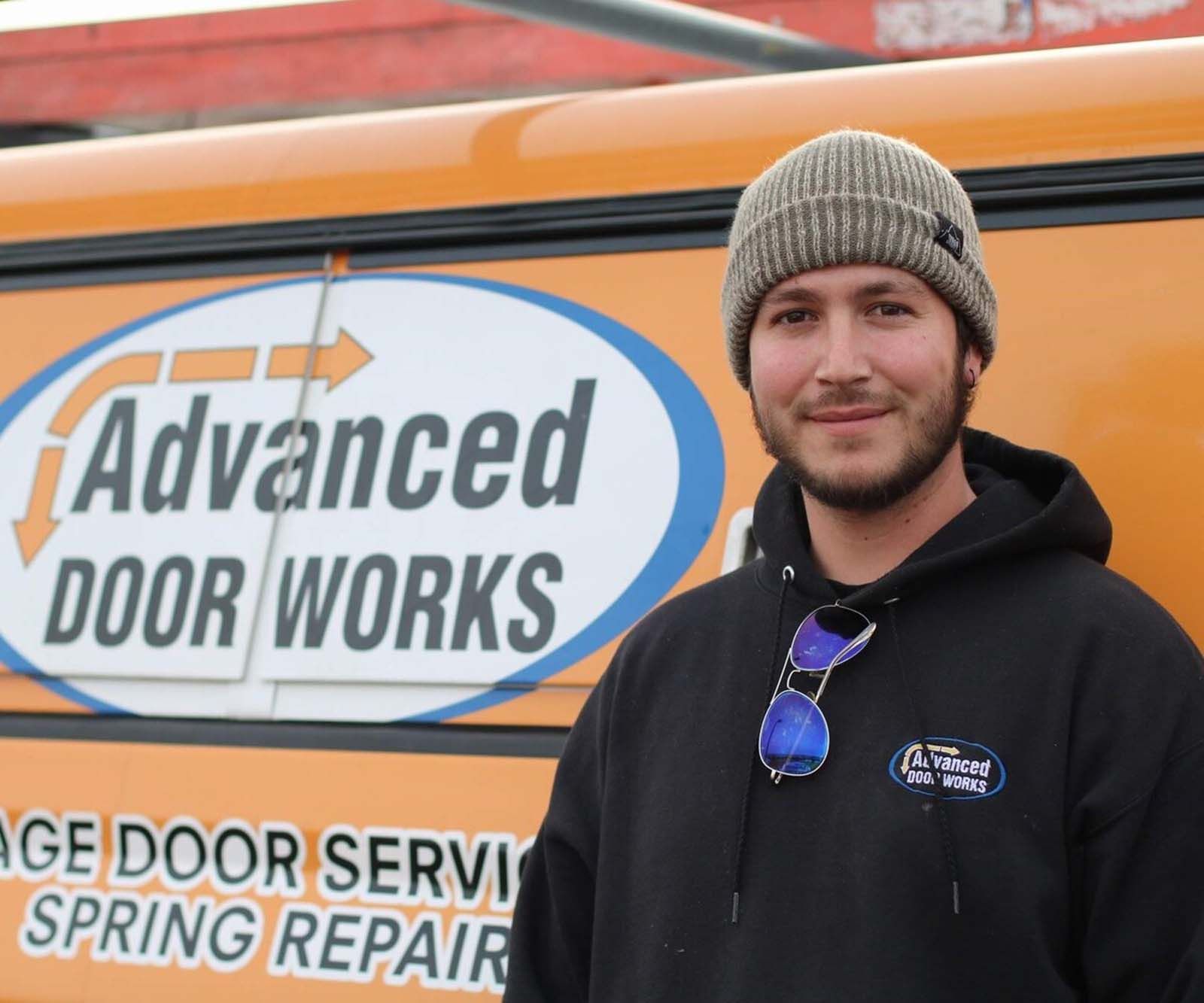 A man standing in front of an orange sign that says advanced door works